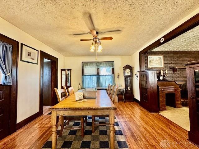 dining room with ceiling fan, a textured ceiling, baseboards, and wood finished floors