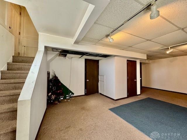 finished basement with a drop ceiling, carpet floors, baseboards, stairway, and rail lighting