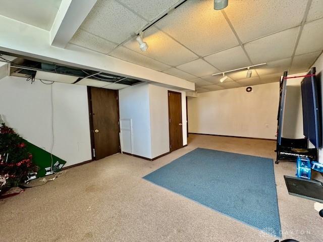 finished below grade area featuring carpet flooring, rail lighting, a paneled ceiling, and baseboards