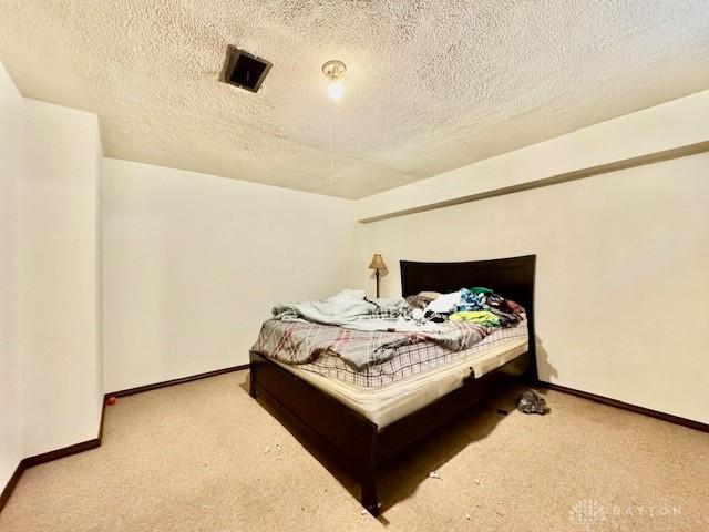 carpeted bedroom featuring a textured ceiling, visible vents, and baseboards