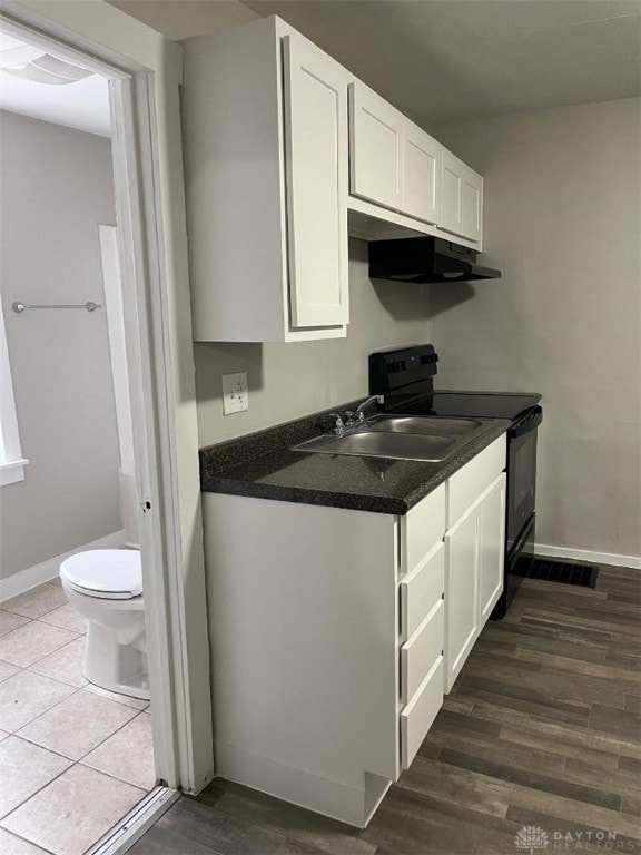 kitchen featuring baseboards, black electric range, under cabinet range hood, white cabinetry, and a sink