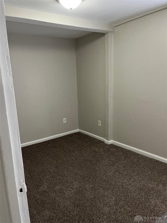 unfurnished room featuring dark colored carpet and baseboards