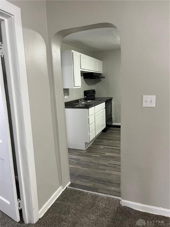 kitchen featuring arched walkways, white cabinets, baseboards, dark countertops, and black range with electric cooktop