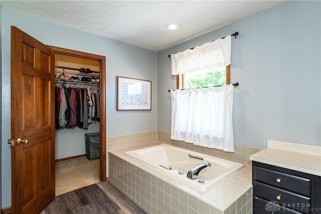 bathroom featuring a textured ceiling, wood finished floors, a garden tub, and a walk in closet