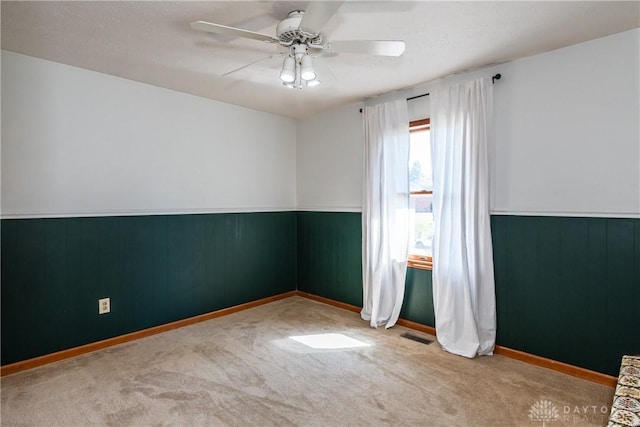 carpeted spare room featuring wainscoting, ceiling fan, and visible vents