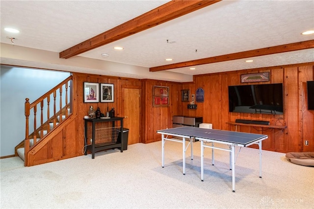 rec room with wood walls, a textured ceiling, beam ceiling, and light colored carpet