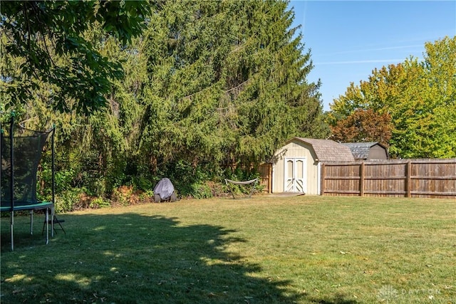 view of yard with a trampoline, an outbuilding, fence, and a shed