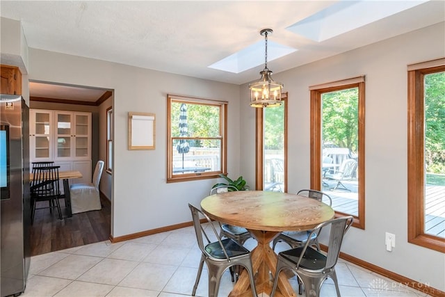 dining room with a skylight, an inviting chandelier, baseboards, and light tile patterned floors