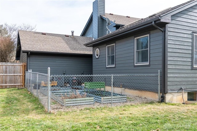 back of house featuring a lawn, a chimney, a vegetable garden, and fence