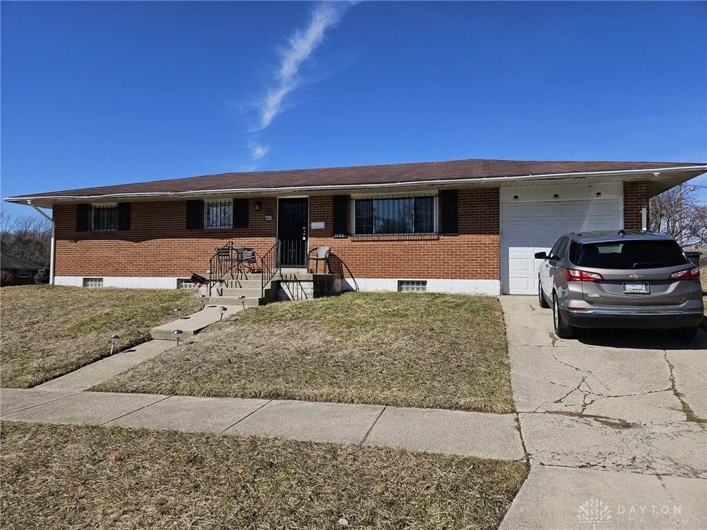 ranch-style house with a front yard, concrete driveway, brick siding, and an attached garage