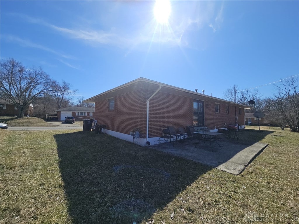 view of side of home with a patio area, brick siding, and a yard