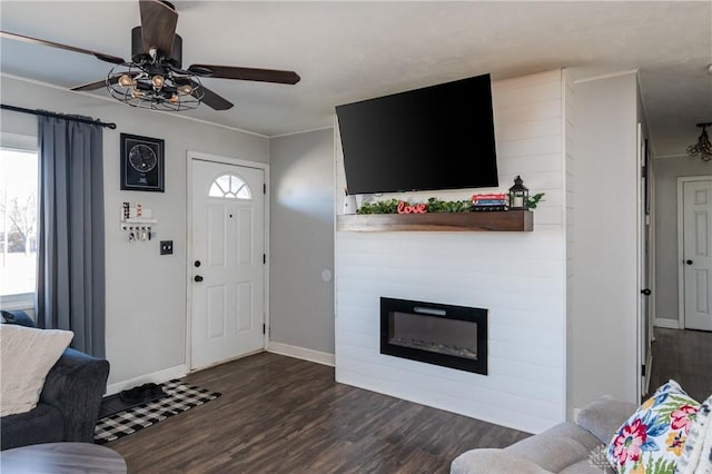 living room featuring ornamental molding, a large fireplace, ceiling fan, wood finished floors, and baseboards