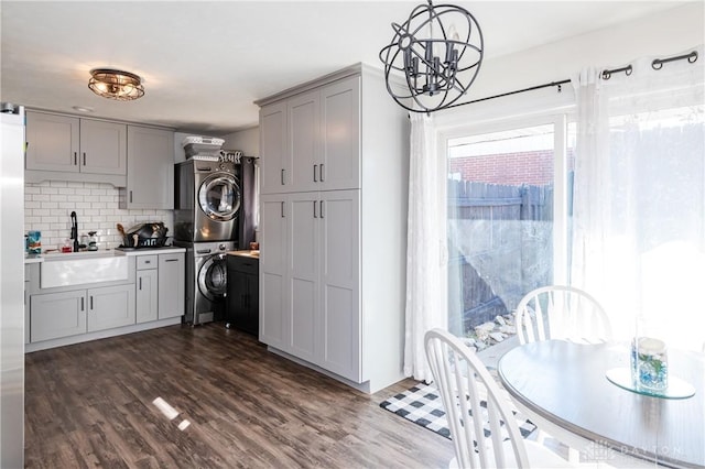 kitchen featuring tasteful backsplash, gray cabinets, dark wood-type flooring, a sink, and stacked washing maching and dryer