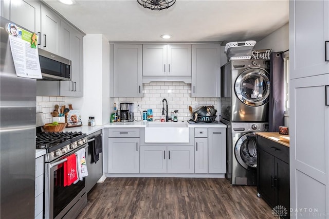 kitchen featuring stacked washer and clothes dryer, light countertops, stainless steel appliances, gray cabinetry, and a sink