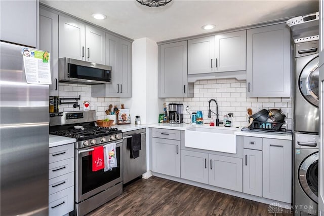 kitchen with stainless steel appliances, stacked washer / drying machine, gray cabinets, light countertops, and a sink