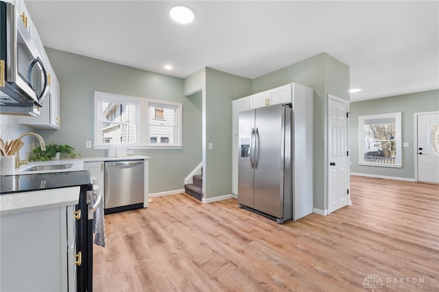 kitchen featuring light wood finished floors, baseboards, white cabinets, stainless steel appliances, and a sink