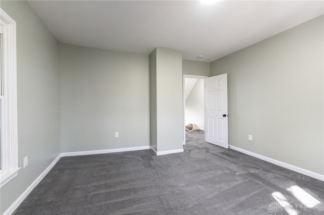 unfurnished bedroom with dark carpet and baseboards