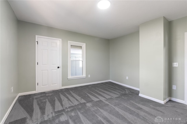 empty room featuring dark colored carpet and baseboards