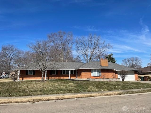 single story home with a garage, driveway, a chimney, and a front yard