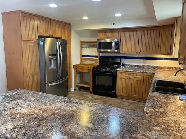 kitchen featuring appliances with stainless steel finishes, dark stone counters, a sink, and recessed lighting