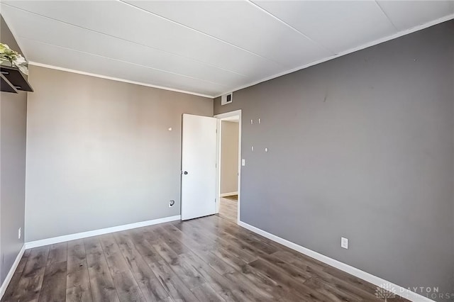 spare room with visible vents, baseboards, wood finished floors, and ornamental molding