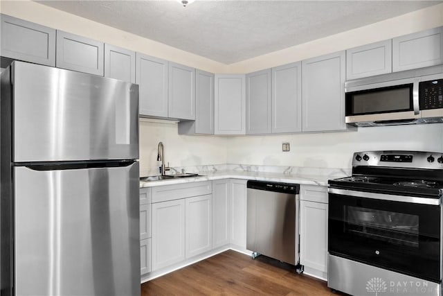 kitchen featuring appliances with stainless steel finishes, dark wood-type flooring, light stone countertops, a textured ceiling, and a sink