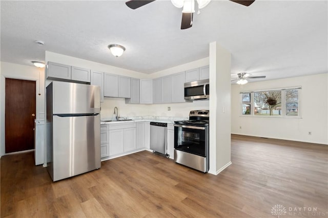 kitchen with light countertops, gray cabinetry, appliances with stainless steel finishes, a sink, and wood finished floors