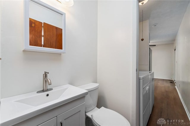 bathroom featuring toilet, washing machine and dryer, wood finished floors, and vanity