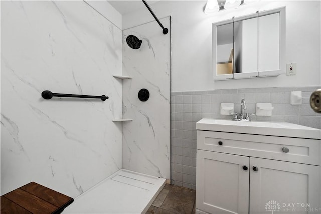 full bath with a marble finish shower, tile walls, and vanity