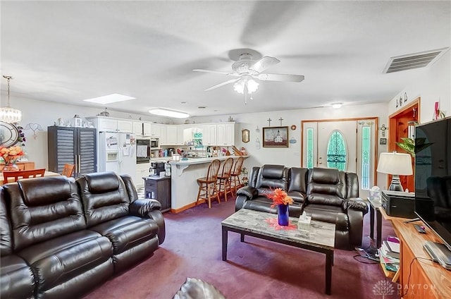 carpeted living room featuring a skylight, visible vents, and ceiling fan with notable chandelier