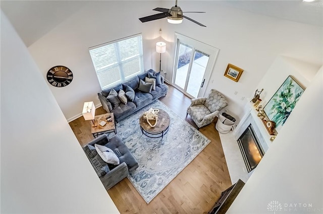 living room featuring ceiling fan, high vaulted ceiling, wood finished floors, and a glass covered fireplace