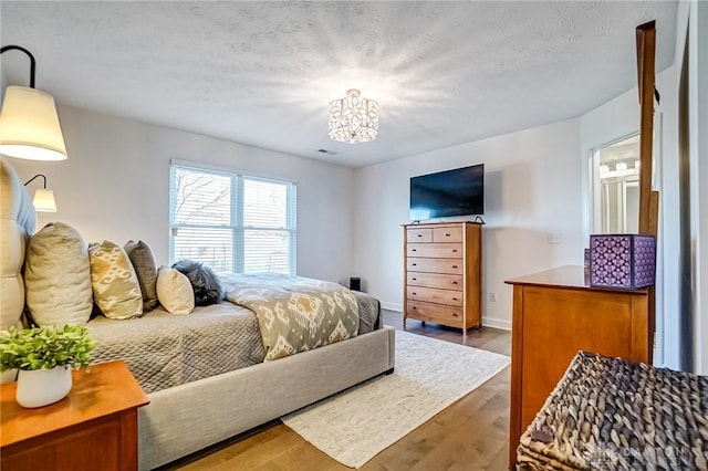 bedroom featuring a chandelier, visible vents, a textured ceiling, and wood finished floors