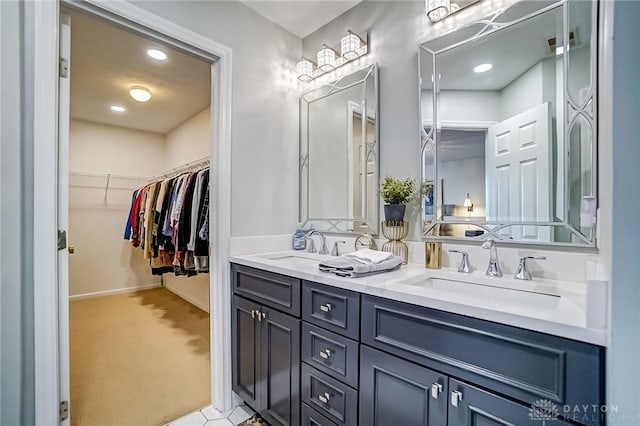 bathroom with double vanity, a sink, a walk in closet, and baseboards