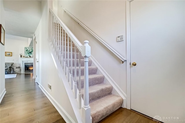 stairs with a lit fireplace, wood finished floors, visible vents, and baseboards