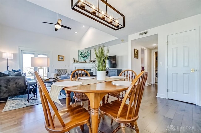 dining space featuring visible vents, a ceiling fan, lofted ceiling, wood finished floors, and a fireplace