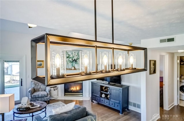 bar featuring wood finished floors, washer / clothes dryer, a glass covered fireplace, and visible vents