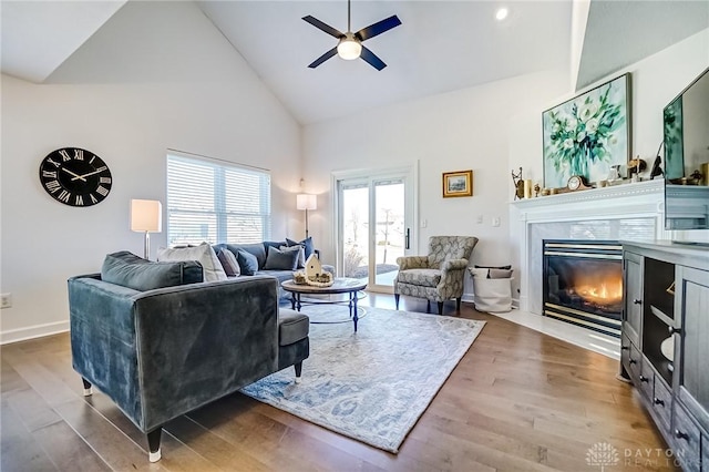 living area with high vaulted ceiling, wood finished floors, a high end fireplace, baseboards, and a ceiling fan