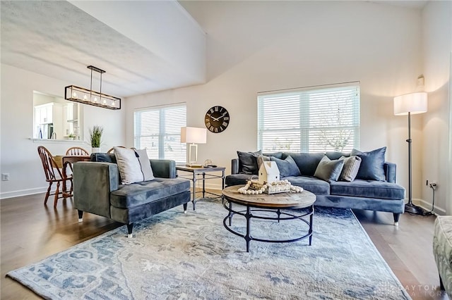 living area featuring an inviting chandelier, a high ceiling, baseboards, and wood finished floors