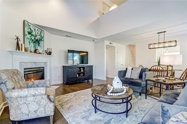 living area with baseboards, a premium fireplace, wood finished floors, an inviting chandelier, and a high ceiling