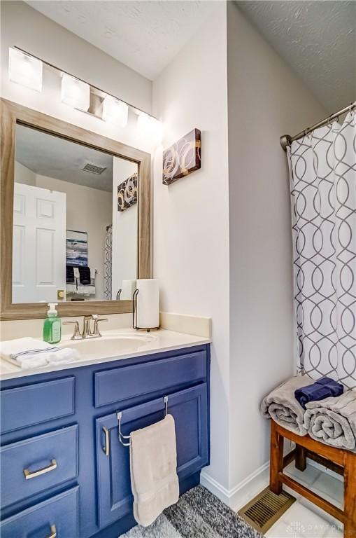 full bath featuring a textured ceiling, vanity, and baseboards