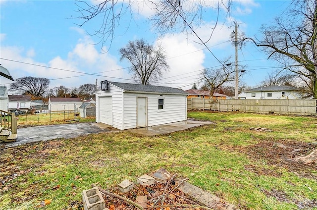 view of yard featuring driveway, a garage, fence, and an outbuilding