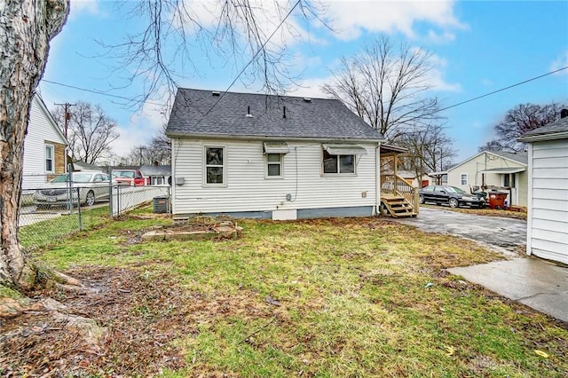 rear view of property featuring roof with shingles, a lawn, and fence