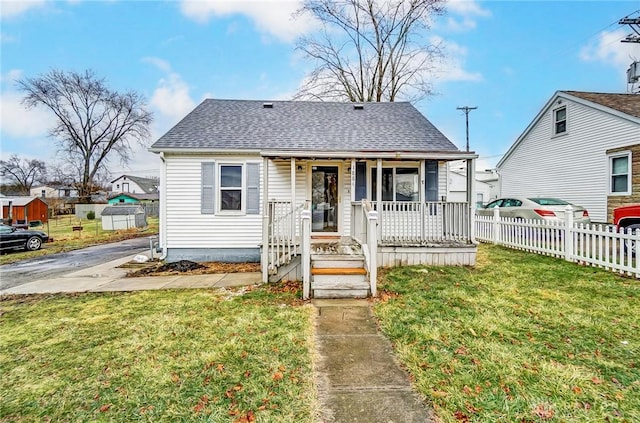 bungalow-style house featuring covered porch, a shingled roof, fence, and a front lawn