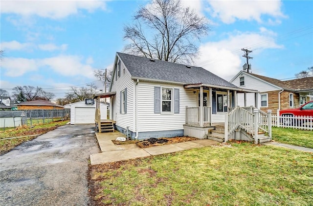 bungalow-style home featuring an outbuilding, fence, concrete driveway, roof with shingles, and a front yard