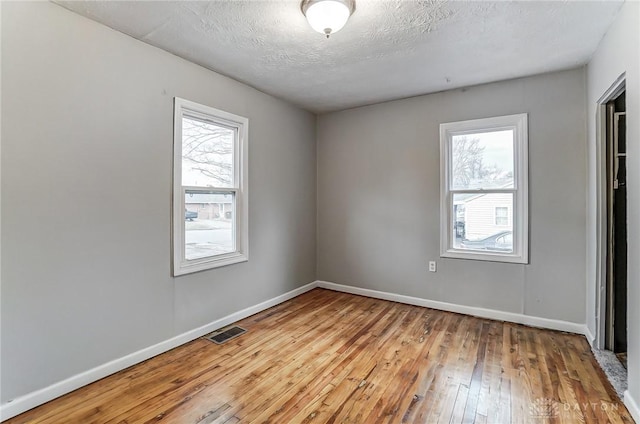 spare room featuring hardwood / wood-style flooring, baseboards, visible vents, and a textured ceiling