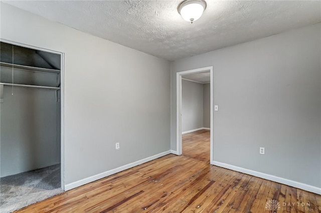 unfurnished bedroom with a closet, baseboards, wood-type flooring, and a textured ceiling