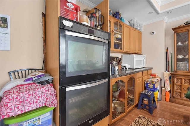 kitchen with white microwave, dobule oven black, ornamental molding, light wood-type flooring, and glass insert cabinets