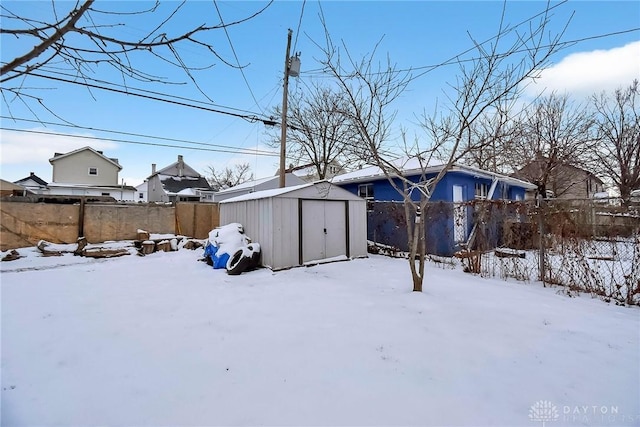 snowy yard with a storage unit, an outdoor structure, and a fenced backyard