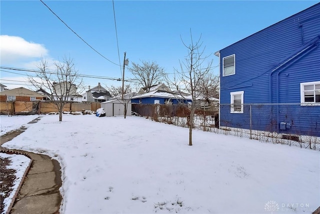 snowy yard with a fenced backyard, a residential view, an outdoor structure, and a shed