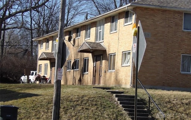 view of property exterior with a shingled roof, a lawn, and brick siding